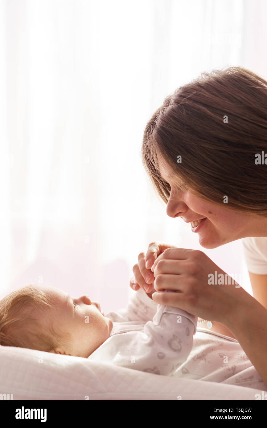 Un neonato è sdraiato sul letto e la madre si tiene le mani e sorridente Foto Stock