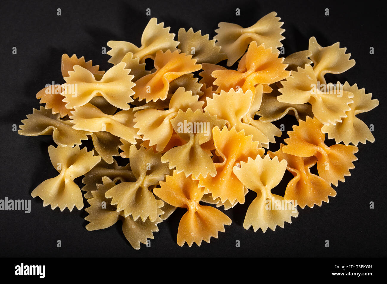 Colorato materie bow tie pasta su sfondo nero. Farfalle di pasta Foto Stock