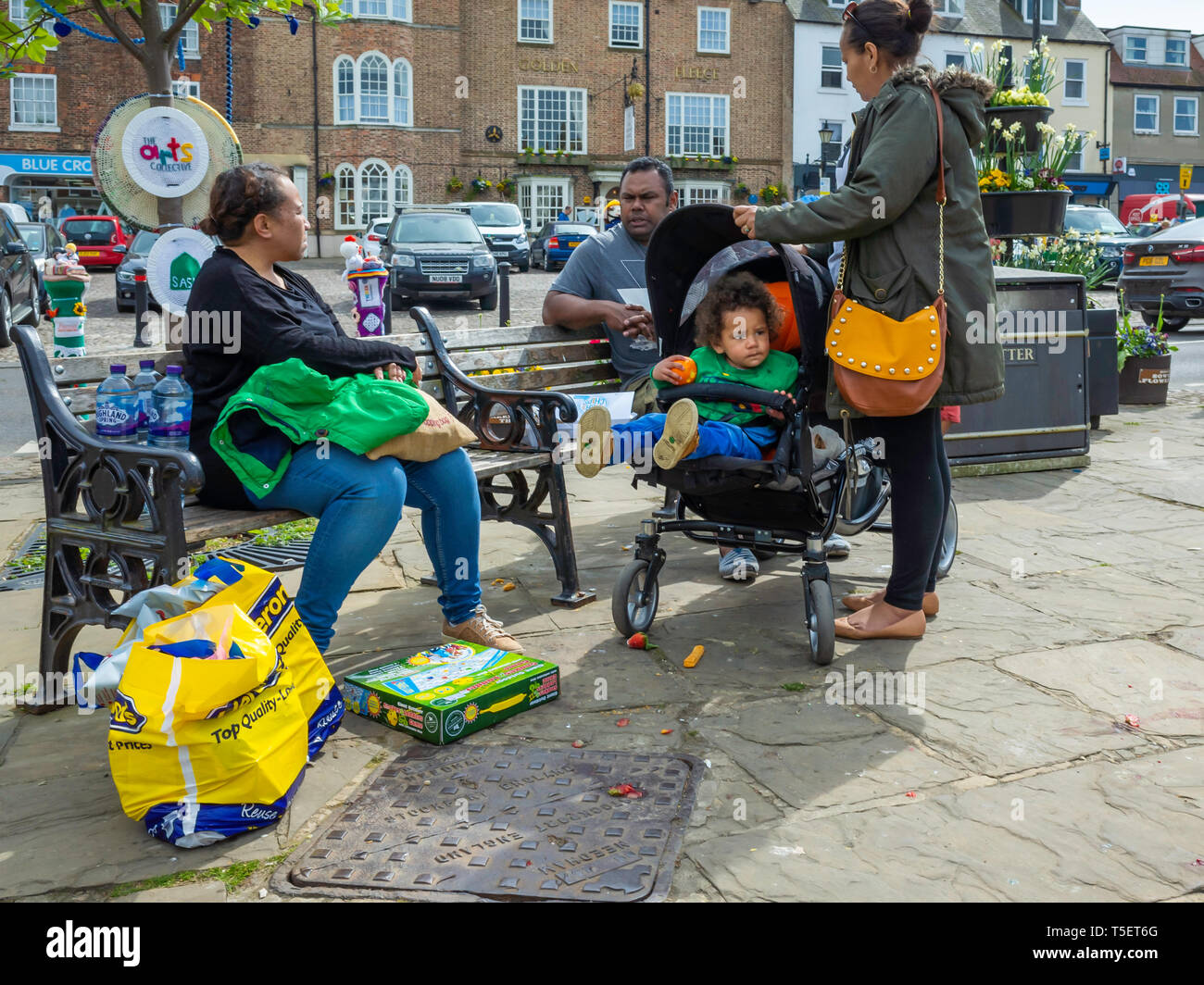 Un etnica Sud famiglia asiatica godendo una pausa dallo shopping e poggiante sulla Piazza del Mercato di Thirsk North Yorkshire Foto Stock