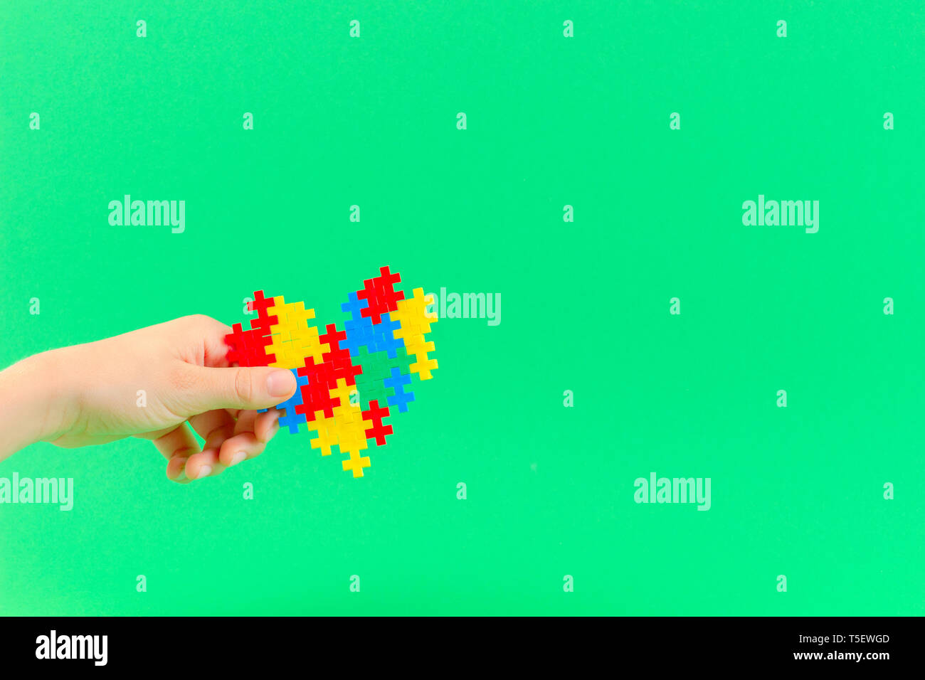 Bambino mano azienda cuore colorati su sfondo verde. Mondo autismo consapevolezza giorno di concetto Foto Stock