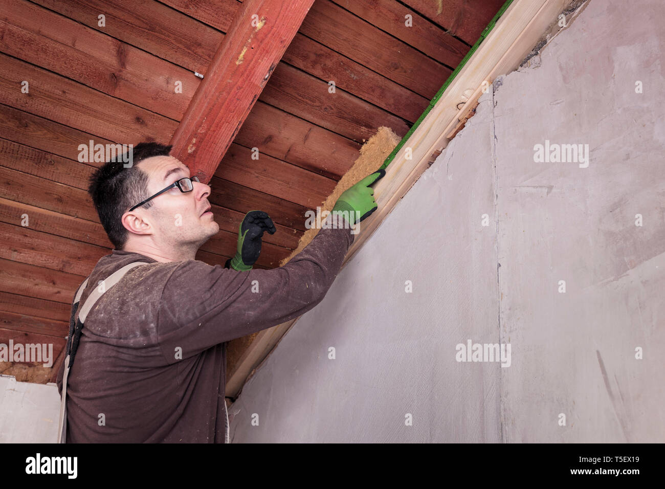 Isolamento del tetto, lavoratore il riempimento di falde del tetto in legno con isolamento in fibra Foto Stock