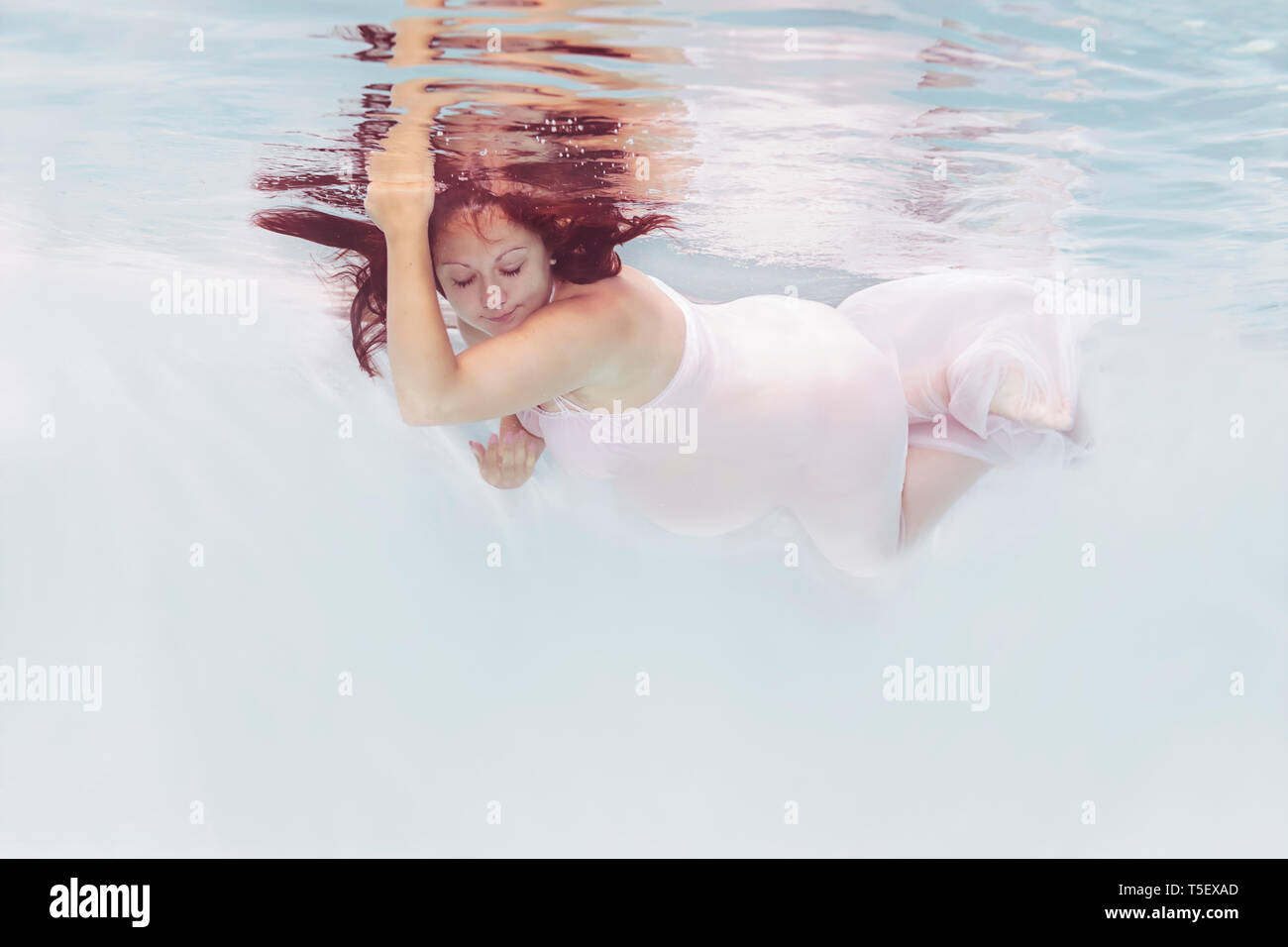 Donna incinta indossando abito bianco sotto l'acqua Foto Stock