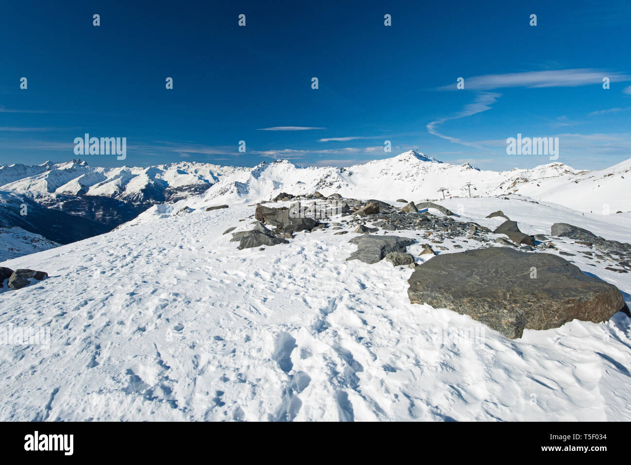 Vista panoramica verso il basso coperto di neve valle nella catena montuosa alpina sul cielo azzurro sfondo con rock in primo piano Foto Stock