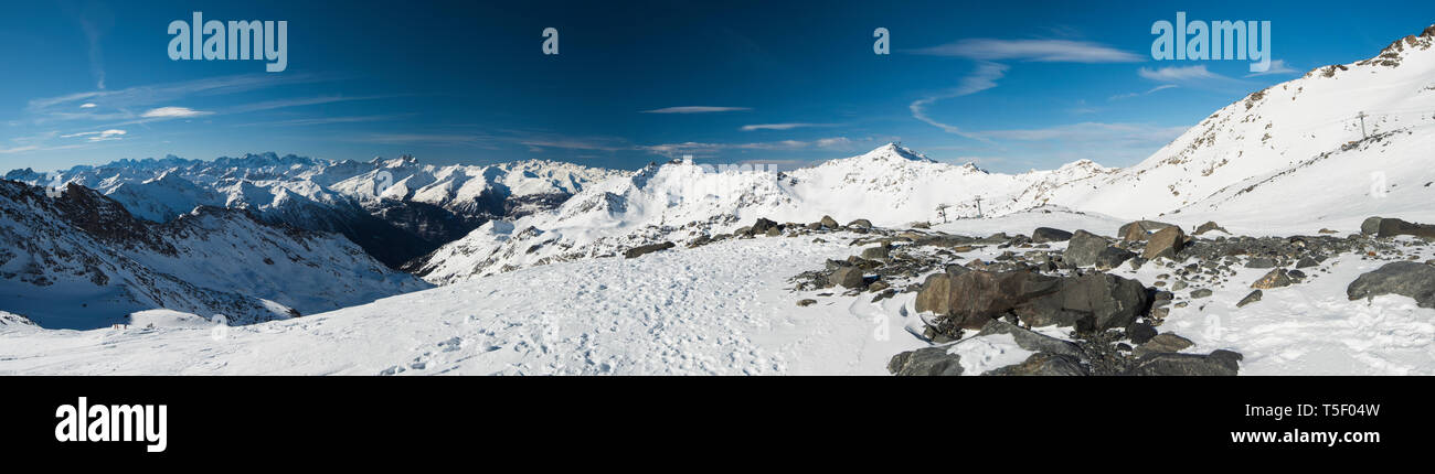 Vista panoramica verso il basso coperto di neve valle nella catena montuosa alpina sul cielo azzurro sfondo con rock in primo piano Foto Stock