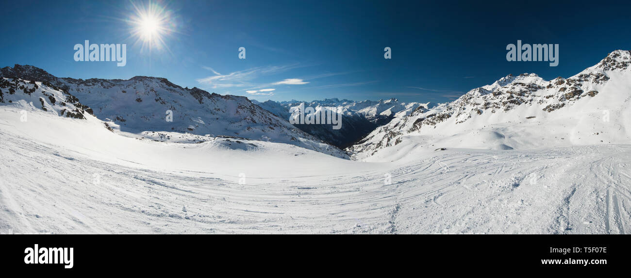 Vista panoramica verso il basso coperto di neve valle nella catena montuosa alpina sul cielo azzurro sfondo con Sun Foto Stock