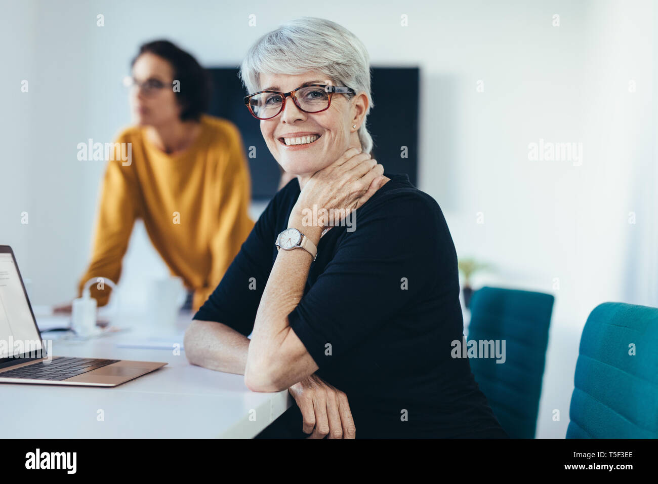Felice imprenditrice seduta a una riunione di lavoro con i colleghi in background. Donna con i colleghi in sala conferenze per partecipare a una riunione. Foto Stock