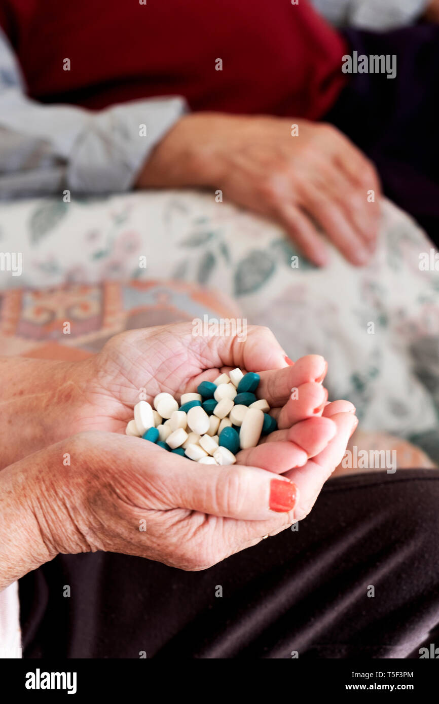 Primo piano di un senior donna caucasica con un mucchio di diverse pillole in mano seduti in un lettino e un anziano uomo caucasico in background Foto Stock