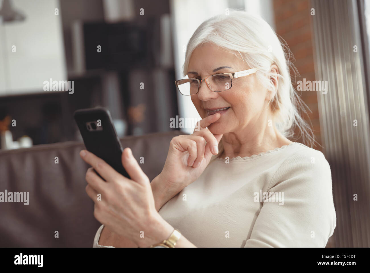 Bella donna senior texting a casa. Il titolare di pensione o di rendita utilizza social media Foto Stock