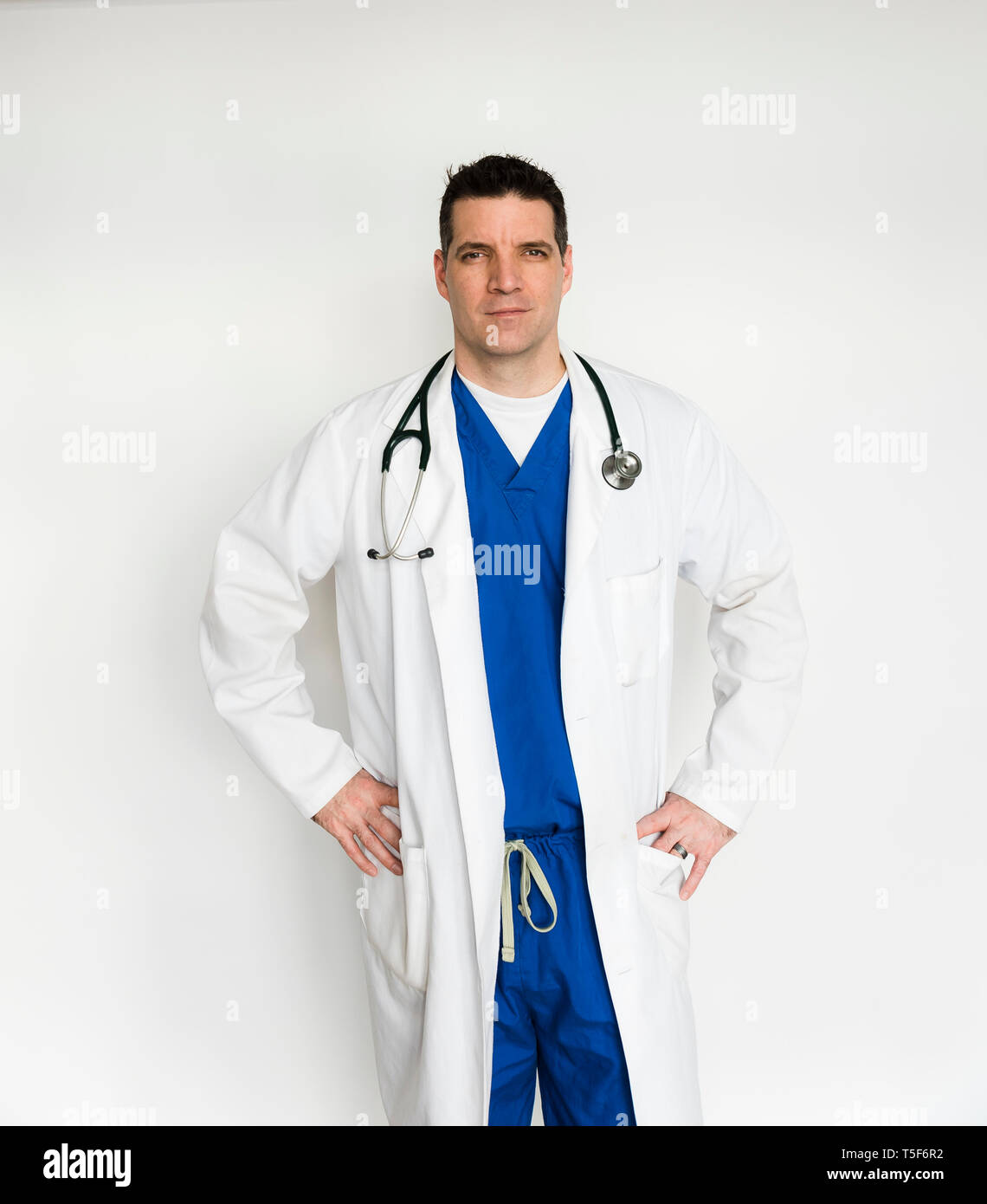 Un medico in camice bianco e scrub in piedi con le mani sui fianchi Foto Stock