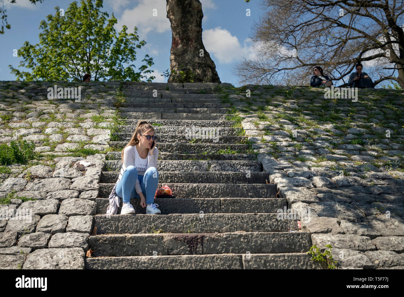 Zemun, Serbia 19 Aprile 2019: giovane donna seduta sulle scale di pietra lungo il Danubio Embankment e parlando tramite smartphone Foto Stock