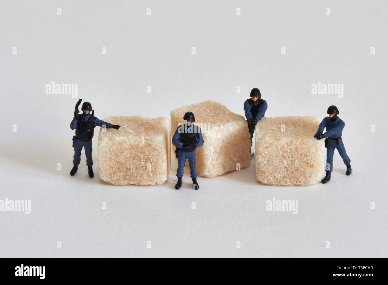 Figurine che rappresentano gli ufficiali di polizia che circondano grumo zucchero: protezione e fissaggio globale del mercato dello zucchero.Caption locale *** Foto Stock