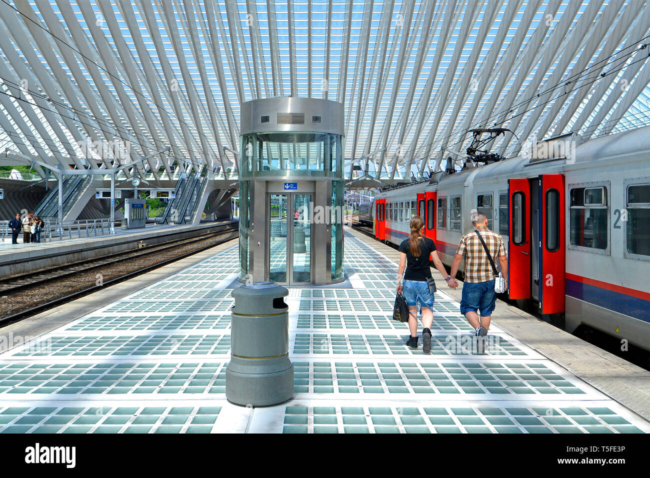 Vista posteriore del giovane uomo e donna giovane tenendo le mani a piedi lungo treno lungo banchina della stazione di Liegi in Belgio moderno edificio ferroviario giorno di estate UE Foto Stock