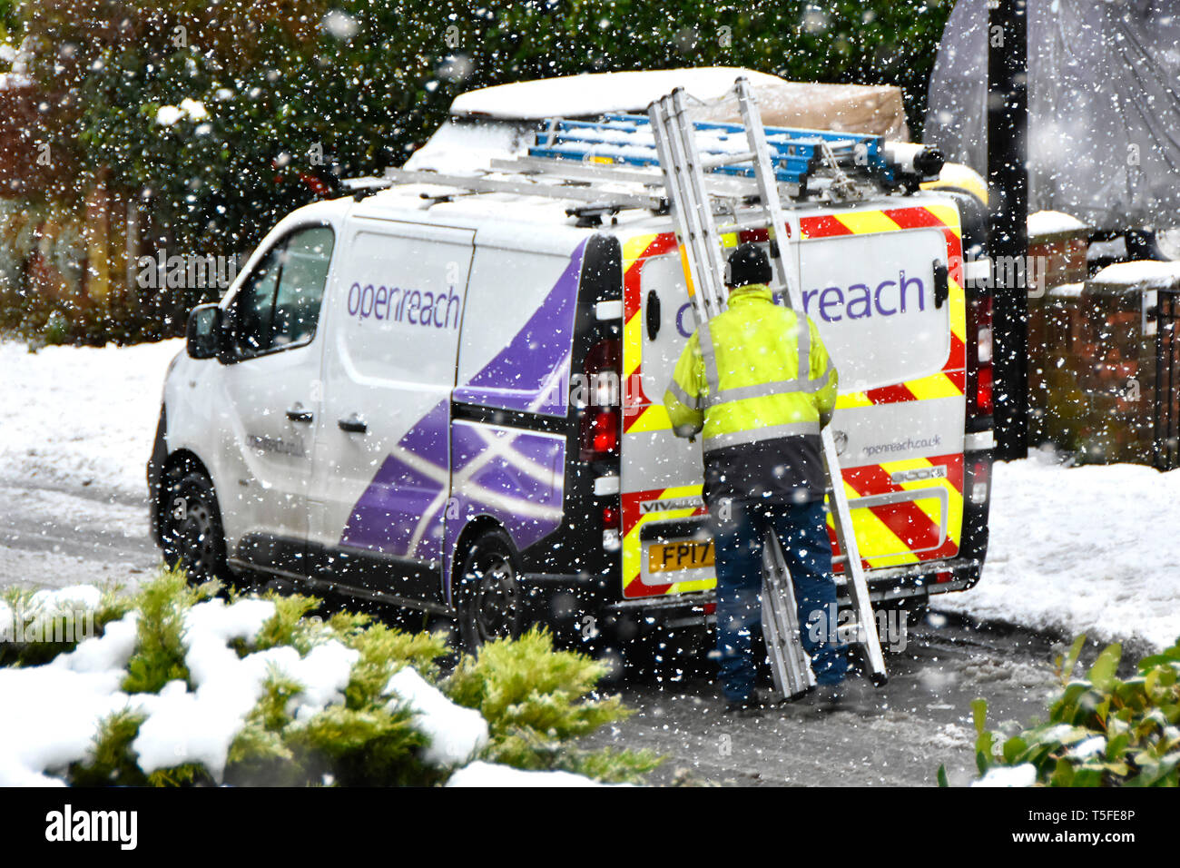Inverno nevoso scena di strada di fiocchi di neve intorno a BT Openreach van & engineer alta vis jacket lavora con scaletta in caduta tempesta di neve England Regno Unito Foto Stock
