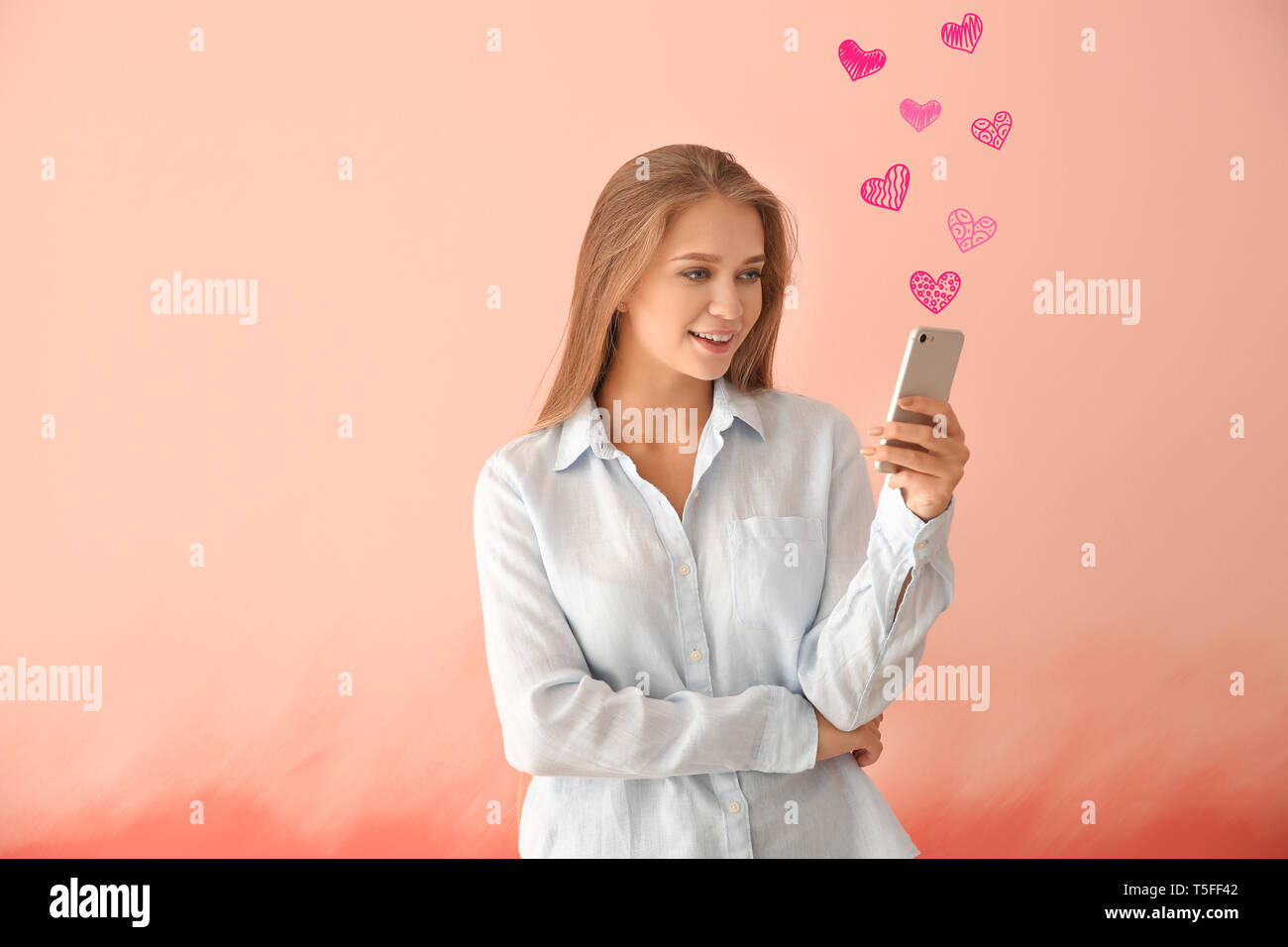 Giovane donna utilizzando il telefono cellulare per incontri online su sfondo rosa Foto Stock