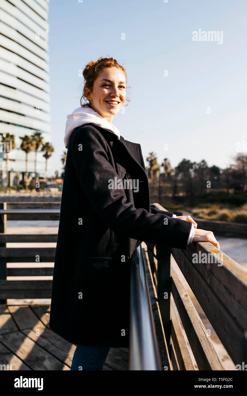 Ritratto di sorridente giovane donna appoggiata contro una recinzione Foto Stock