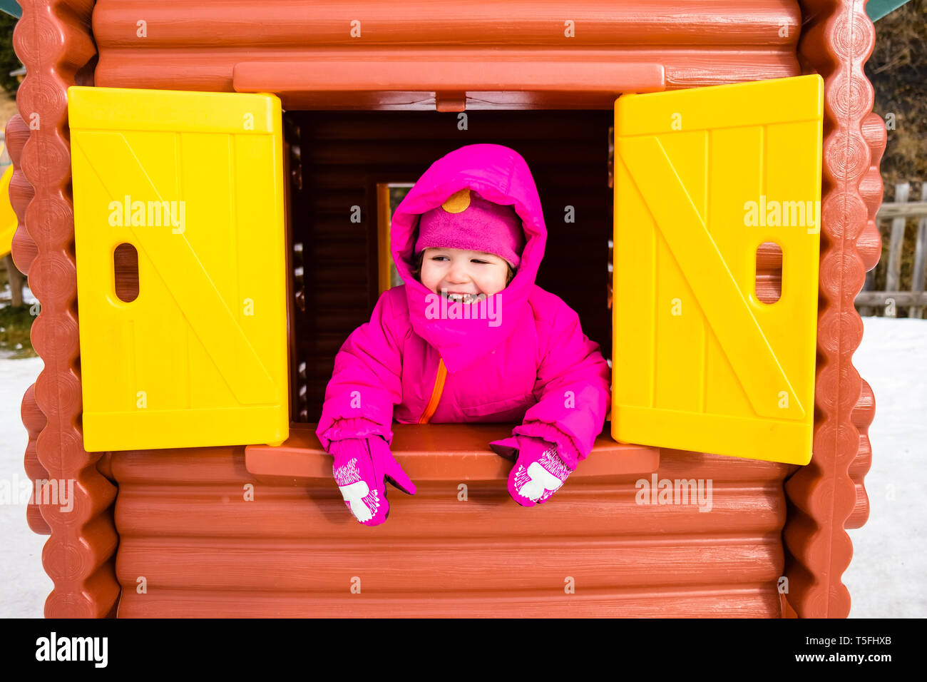 Felice ragazza in rosa cappotto invernale guardando fuori della finestra di un playhouse Foto Stock
