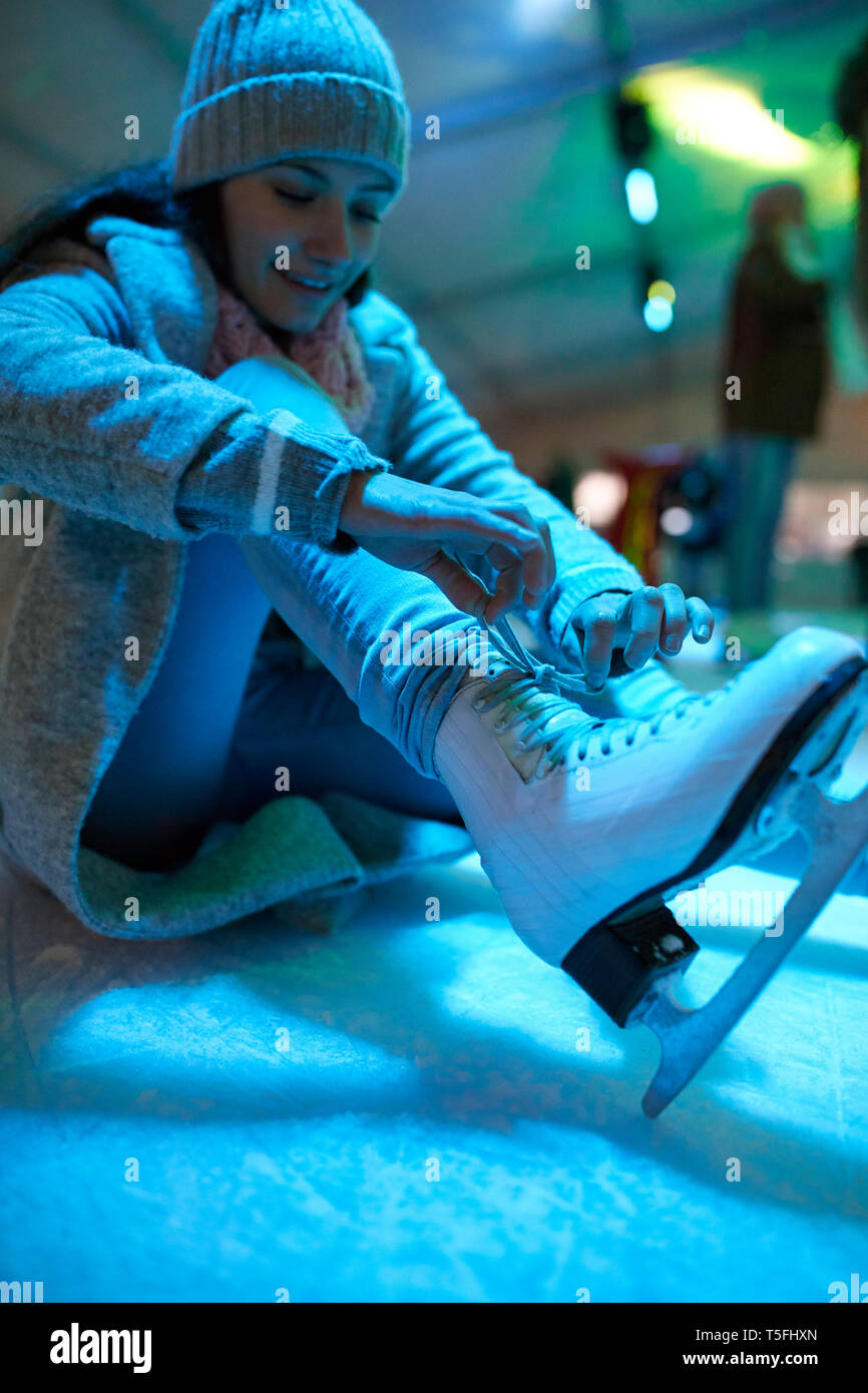Donna seduta sulla pista di pattinaggio su ghiaccio a mettere su pattini da ghiaccio Foto Stock