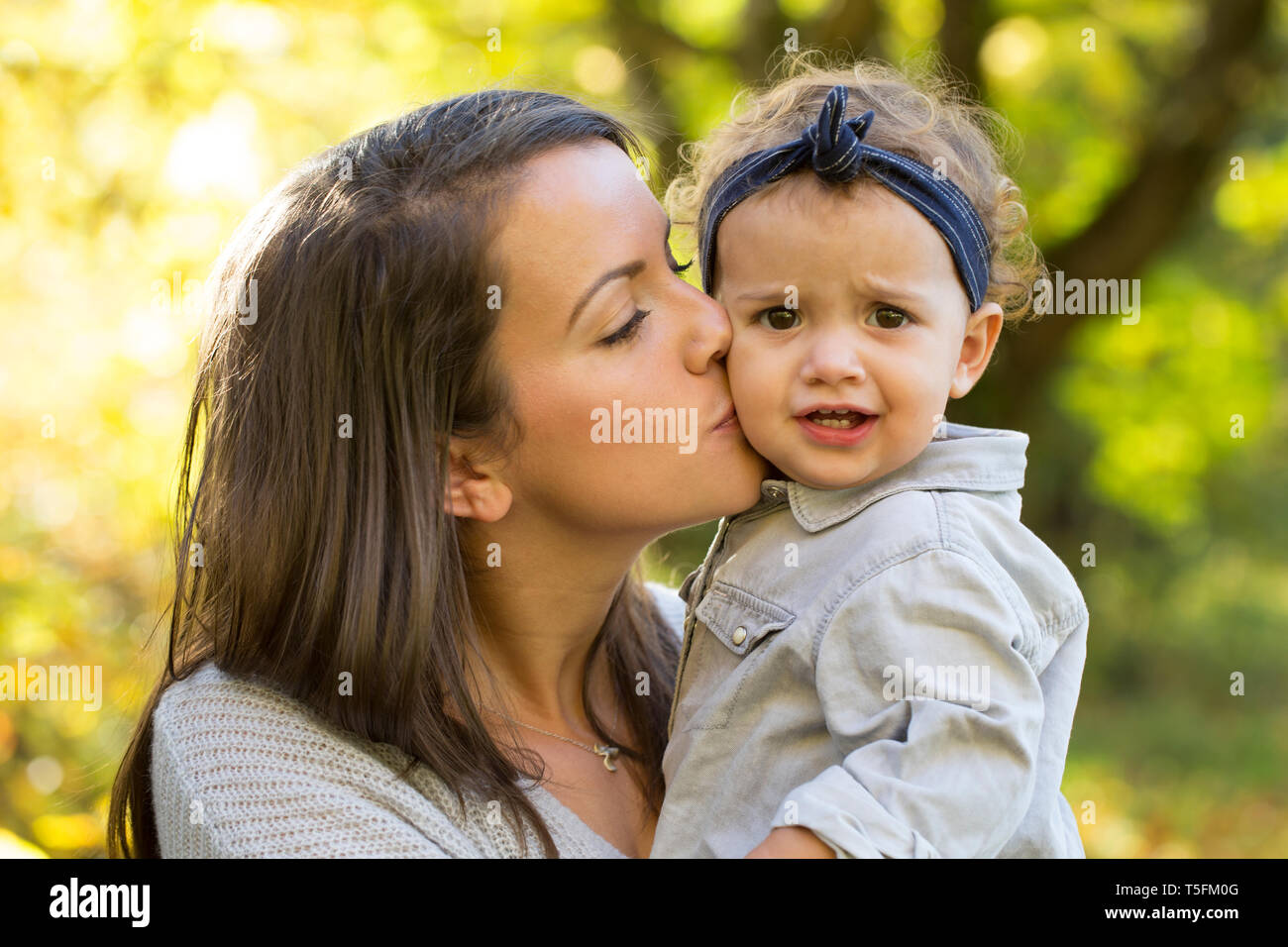 Madre baciare bambina all'aperto in autunno Foto Stock