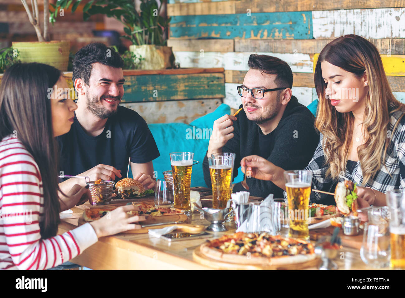 Giovani amici gustando il tempo insieme a mangiare hamburger e pizza al pub alla moda Foto Stock