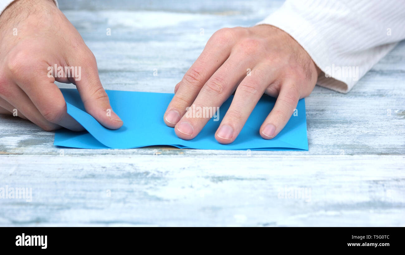 Chiudere fino a mani blu di piegatura del foglio di carta. Foto Stock