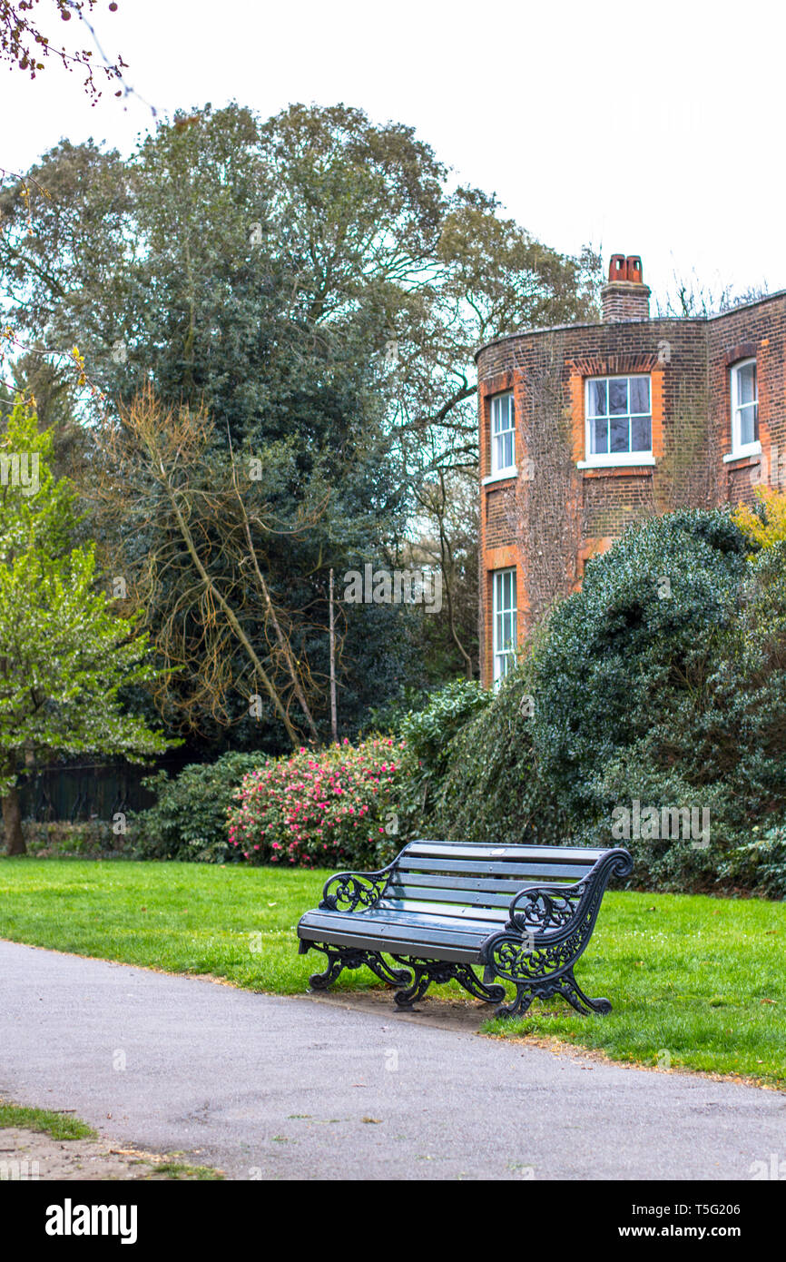 Una panchina nel parco lungo il percorso contro lo sfondo di un classico inglese edificio di mattoni rossi. Luogo ideale per jogging Foto Stock