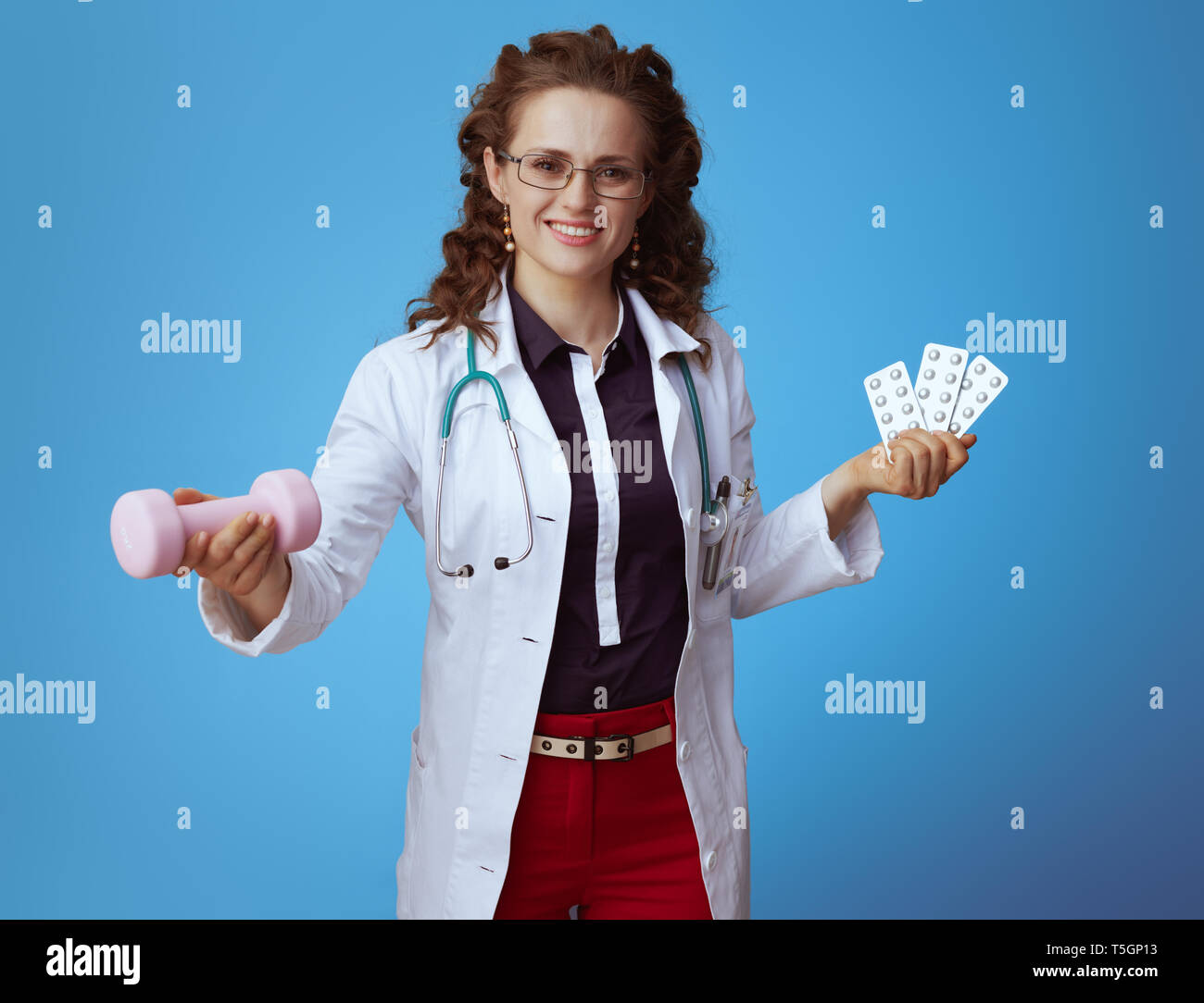 Felice moderno medico donna in bue t-shirt, pantaloni rosso e bianco manto medico dando il manubrio tenendo compresse in blister in altri invece ho Foto Stock