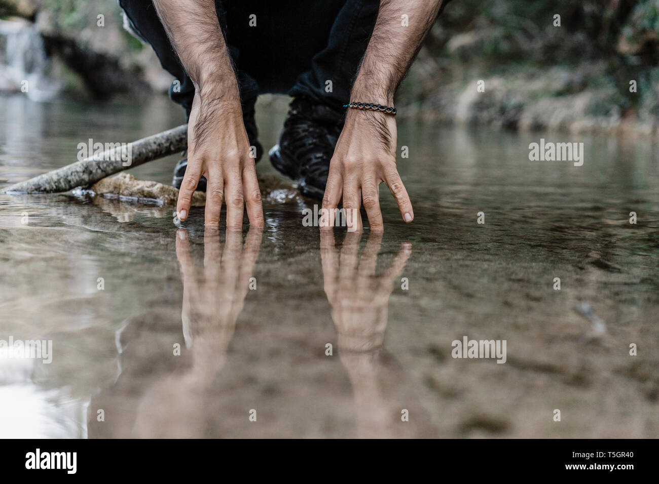 Giovane uomo toccano acqua vicino Cova Simanya, Barcelona, Spagna. Foto Stock