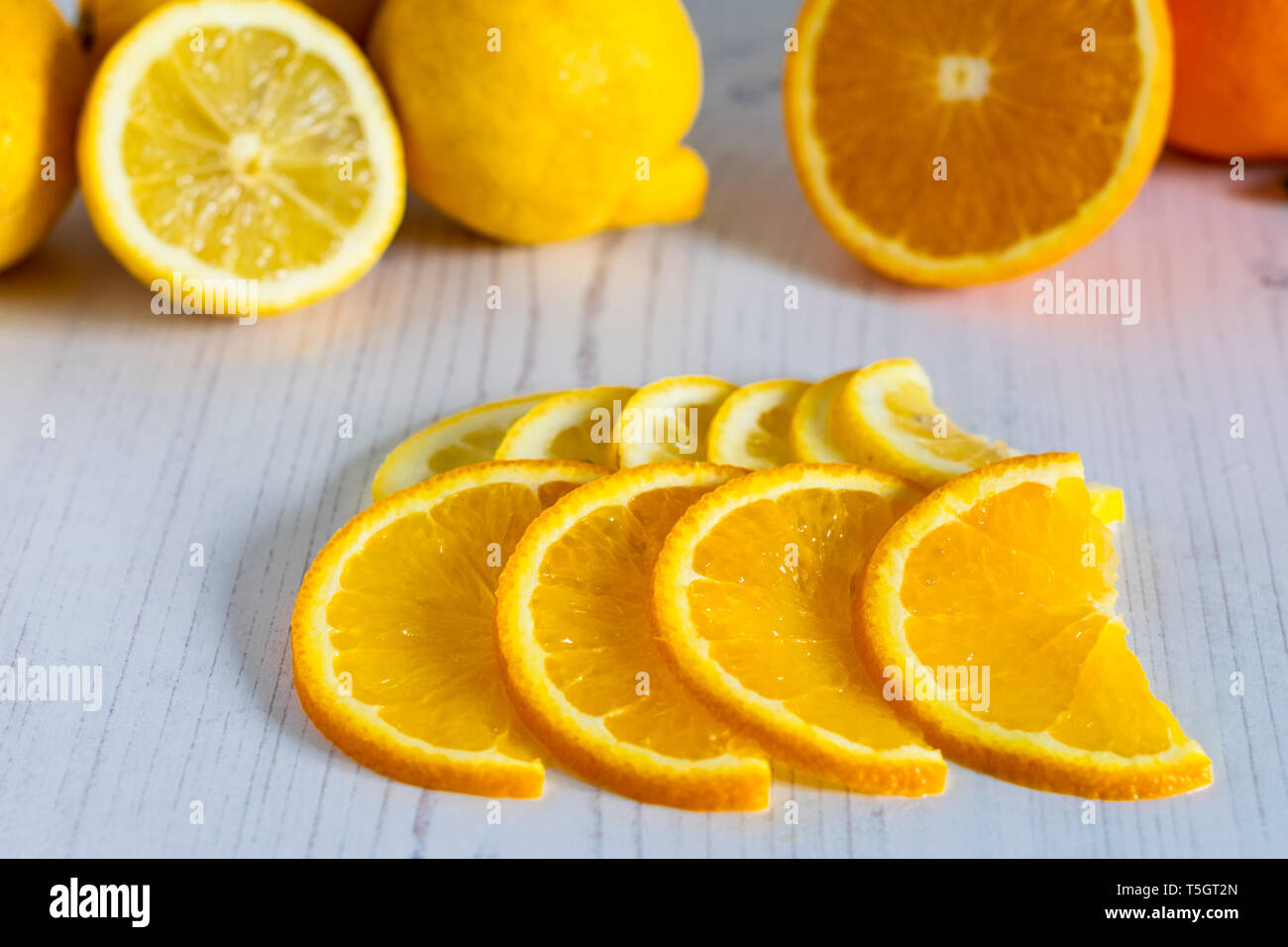 Fette di arancia e limone su uno sfondo chiaro con frutta in background Foto Stock