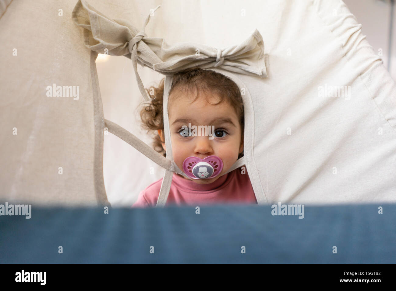 Bambina con succhietto, guardando attraverso wondow di un gioco tenda Foto Stock