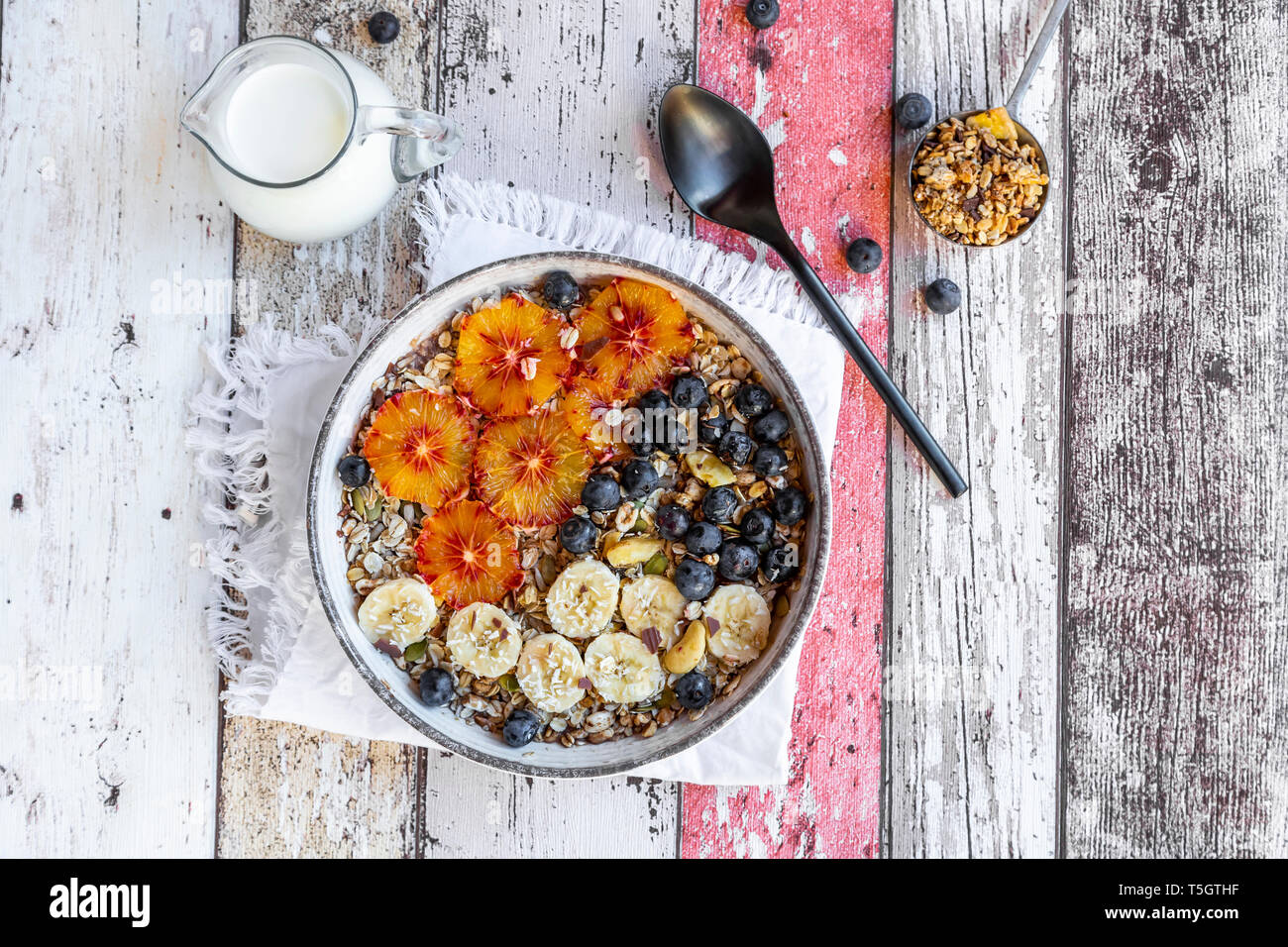 Cereali con banana, mirtilli, Arancio sanguigno, scaglie di cocco e latte Foto Stock