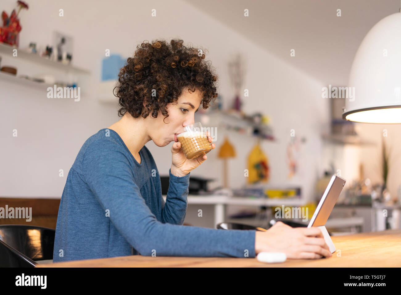 Giovane donna seduta a tavola, utilizzando digitale compressa, bere caffè Foto Stock