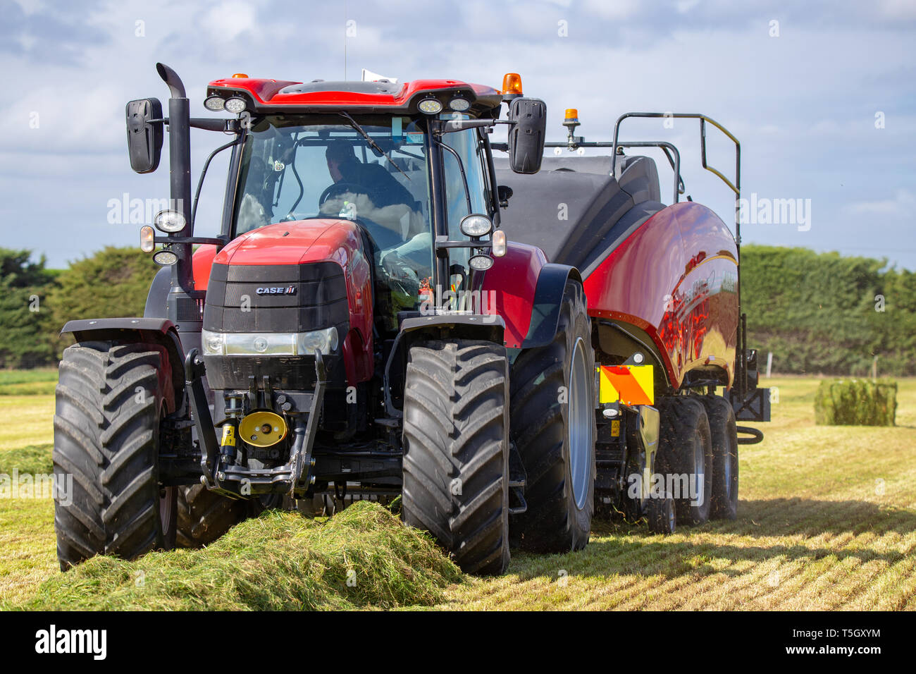 Kirwee, Canterbury, Nuova Zelanda, 27 marzo 2019: un caso di pressa e trattore a lavoro rendendo balle di fieno a sud dell'isola campo agricolo giorni di eventi Foto Stock