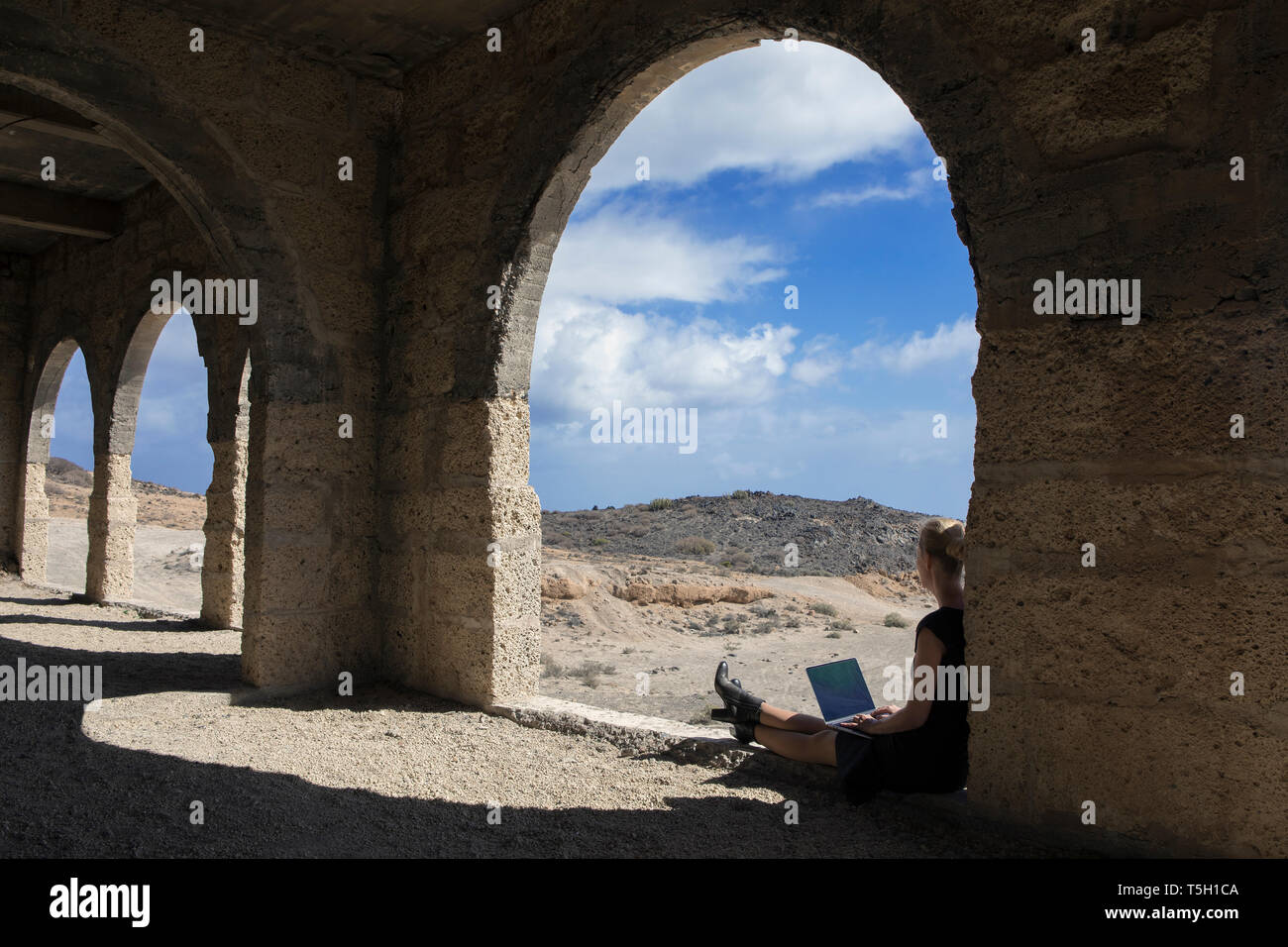 Spagna, Tenerife, Abades, Sanatorio de Abona, donna seduta nella città fantasma edificio utilizzando laptop Foto Stock