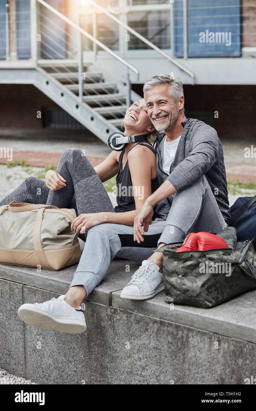 Ridendo uomo maturo e giovane donna con borsa sportiva seduti di fronte palestra Foto Stock