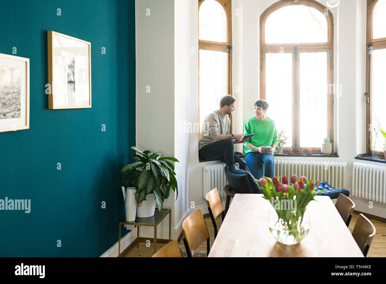 Casual giovane avente una conversazione e seduta alla finestra in appartamento elegante Foto Stock