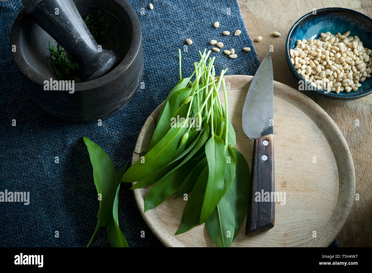 Ramson e coltello sulla tavola di legno, malta e una ciotola di pinoli Foto Stock