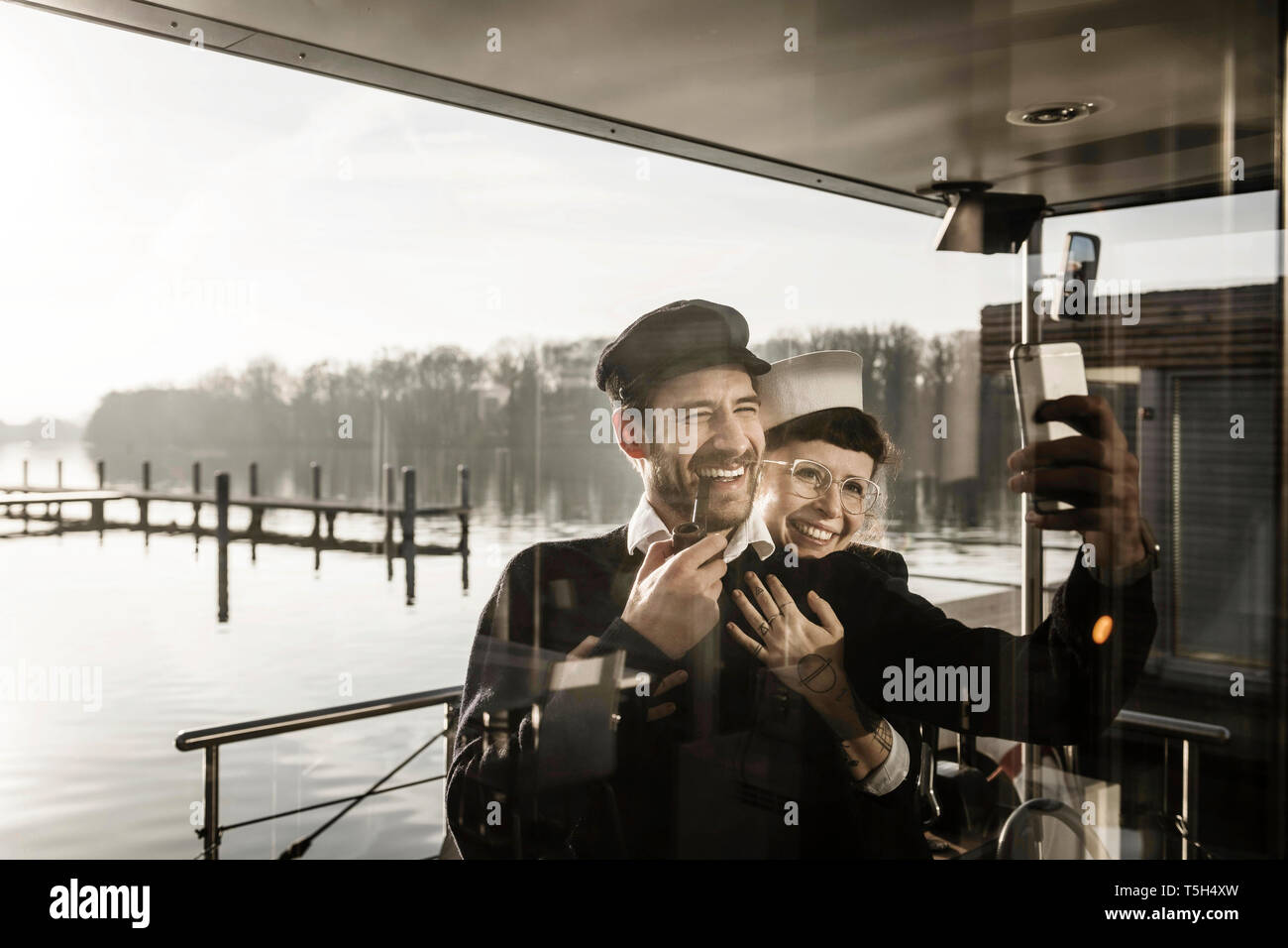 I colleghi lavorando su una casa galleggiante, tenendo selfies come marinaio e capitano Foto Stock