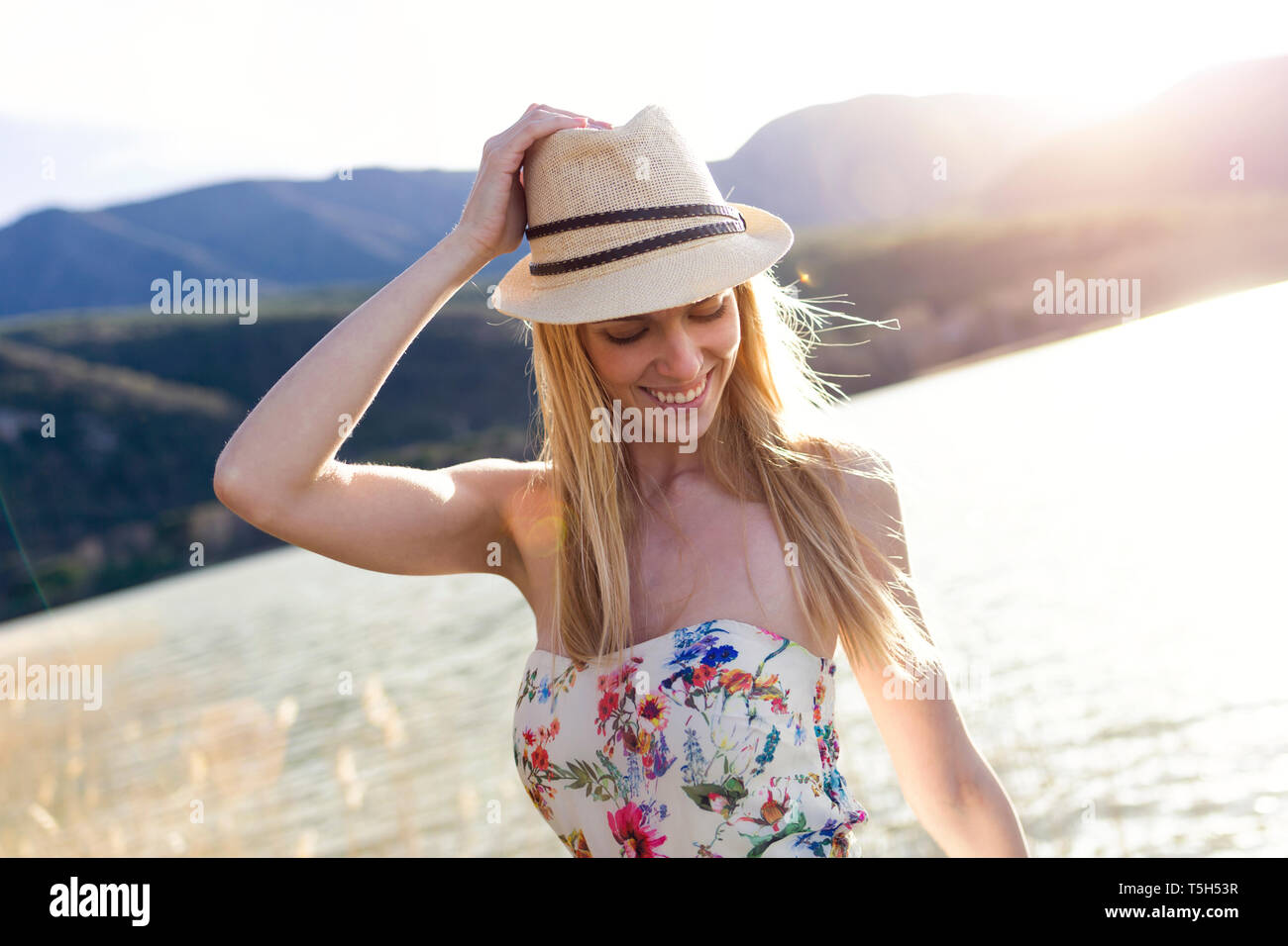 Sorridente giovane donna indossa estate hat e top con disegno floreale di fronte al lago Foto Stock