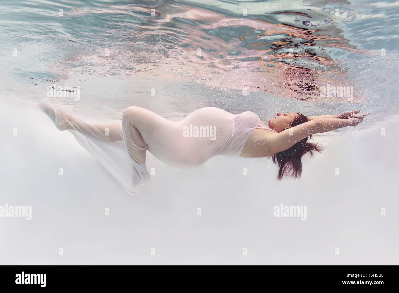 Donna incinta indossando abito bianco sotto l'acqua Foto Stock