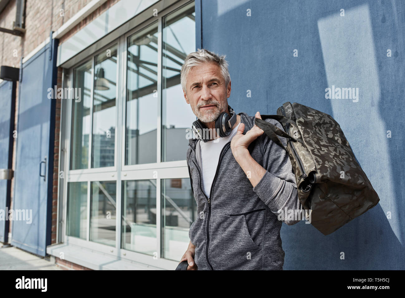 Ritratto di uomo maturo con cuffie e camouflage borsa sportiva di fronte palestra Foto Stock