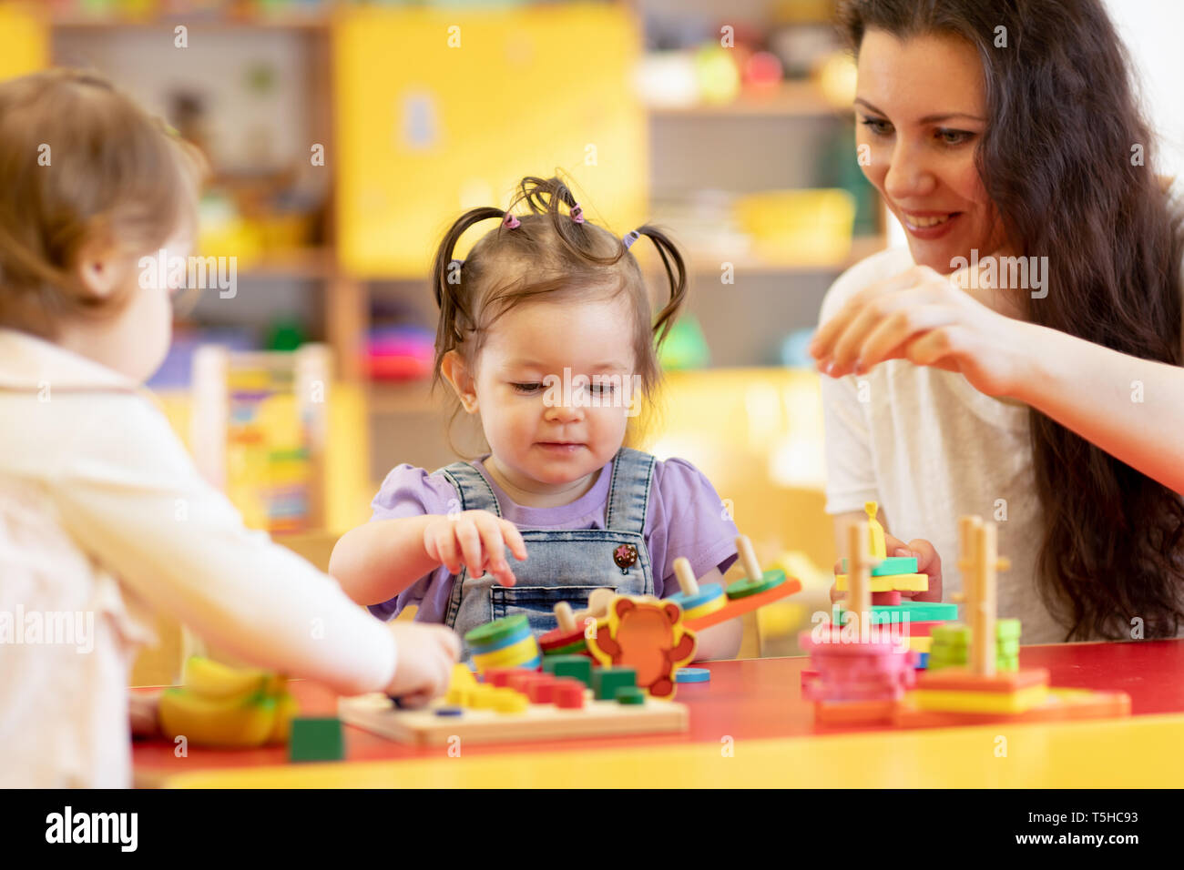 Vivaio bambini giocano con forme e colorato puzzle in legno in un aula montessori. Insegnante di scuola materna contribuisce ai bambini Foto Stock