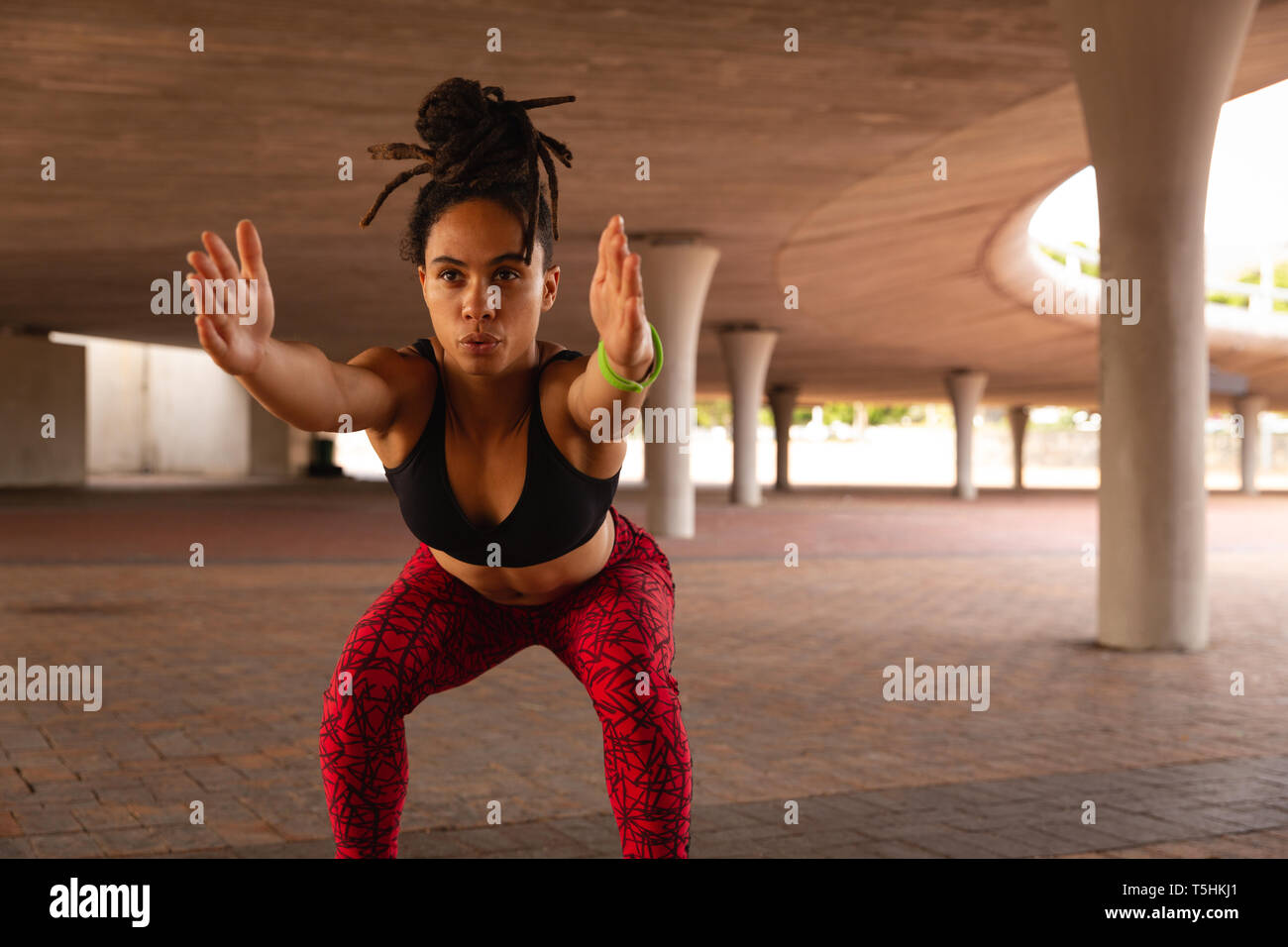 Giovane donna facendo esercizio squat sotto un ponte Foto Stock