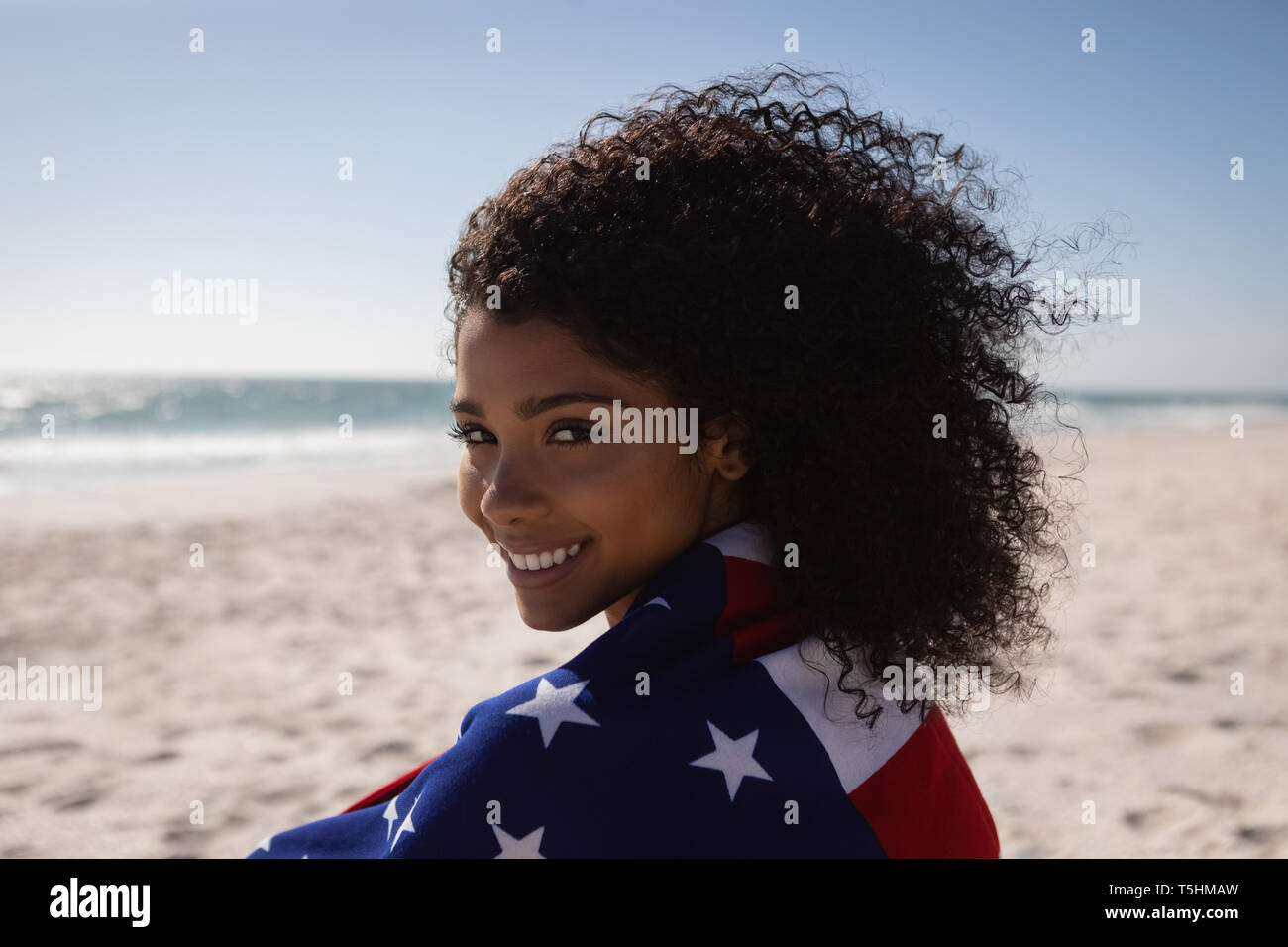 Bella donna holding bandiera americana mentre si sta in piedi in spiaggia in una giornata di sole Foto Stock