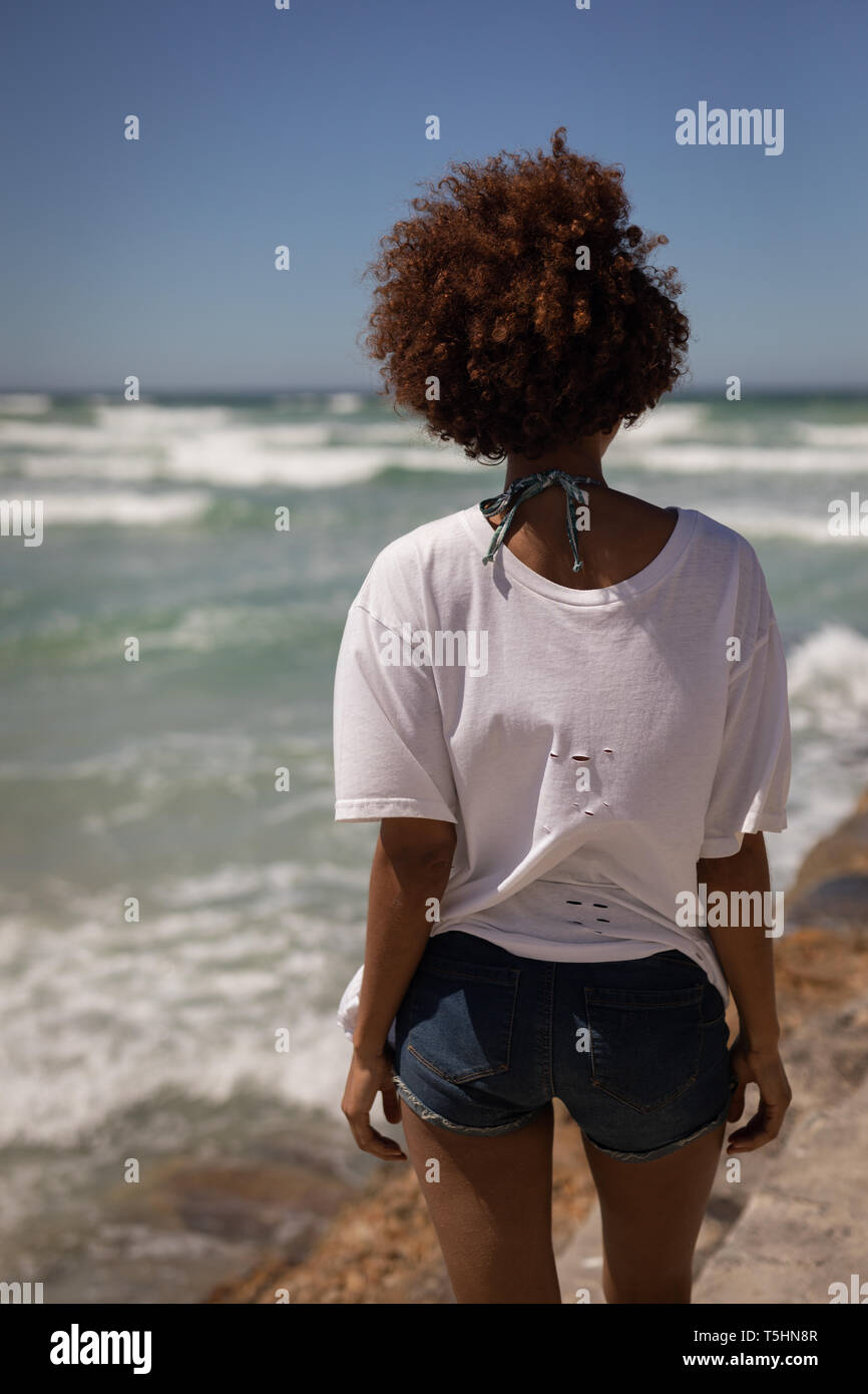 Giovane donna in piedi in spiaggia in una giornata di sole Foto Stock