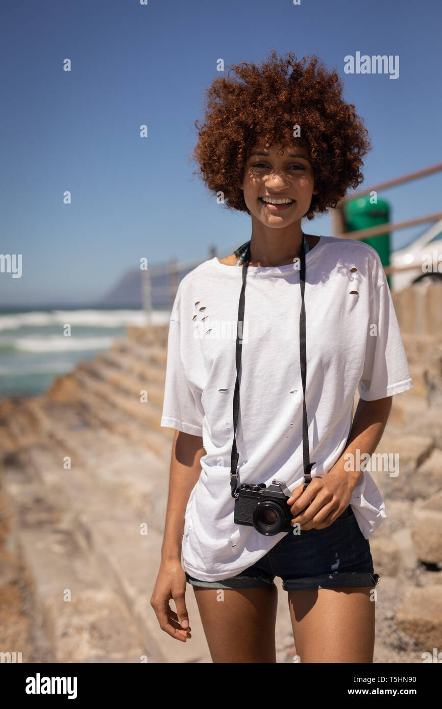 Donna in piedi con la fotocamera in spiaggia in una giornata di sole Foto Stock