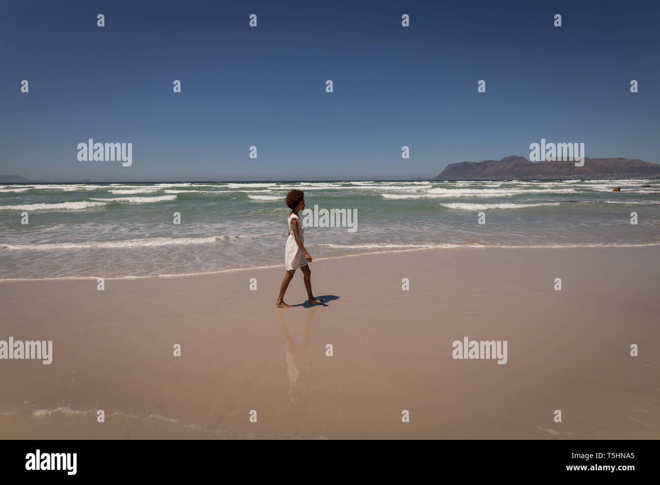 Donna che cammina da sola in spiaggia in una giornata di sole Foto Stock