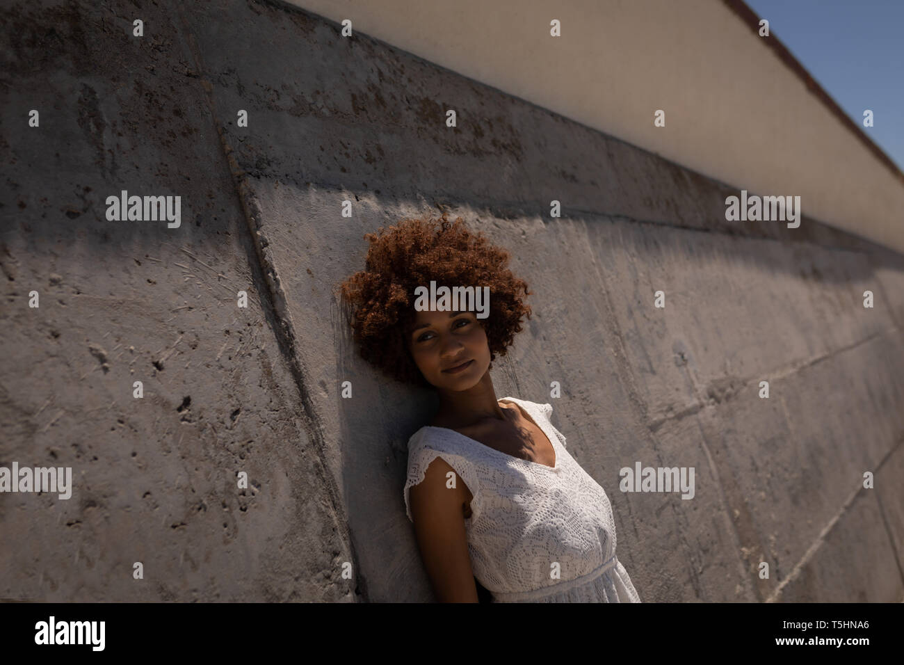 Donna appoggiata contro la parete a beach in una giornata di sole Foto Stock