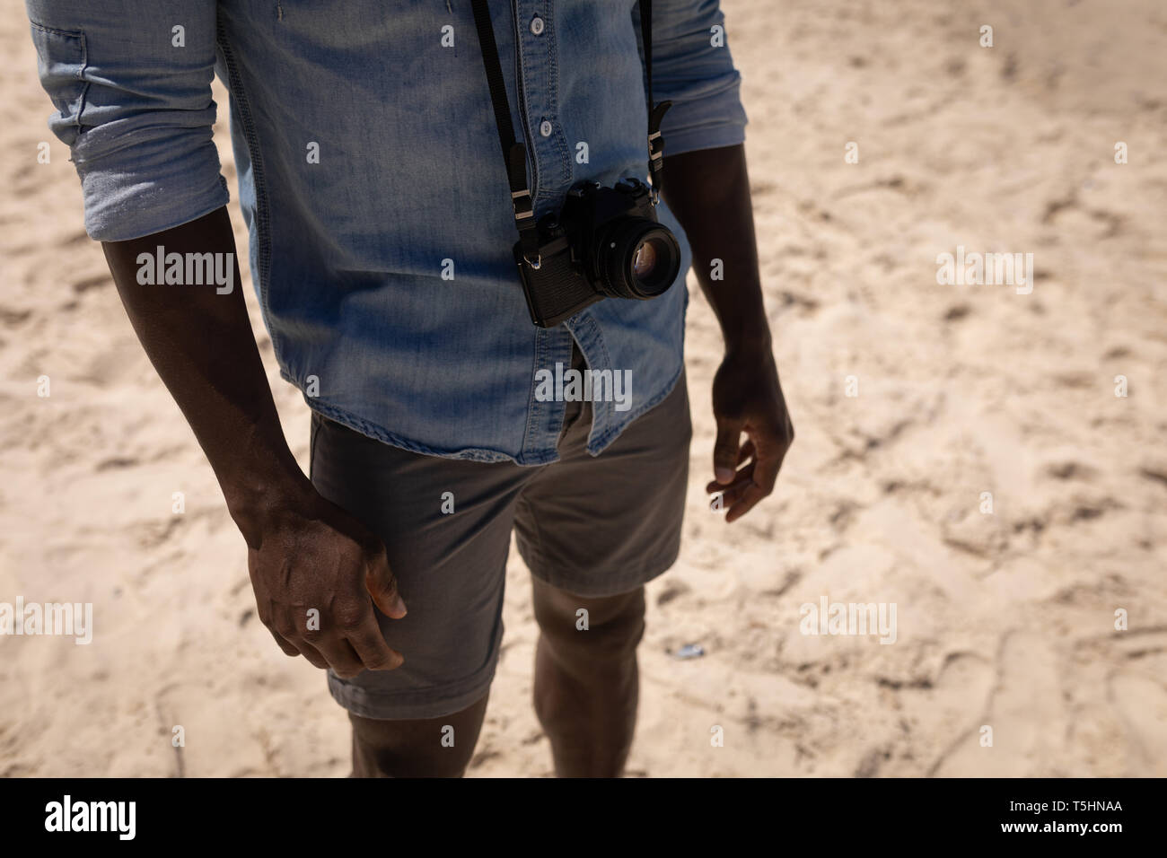 Uomo in piedi con la fotocamera in spiaggia in una giornata di sole Foto Stock