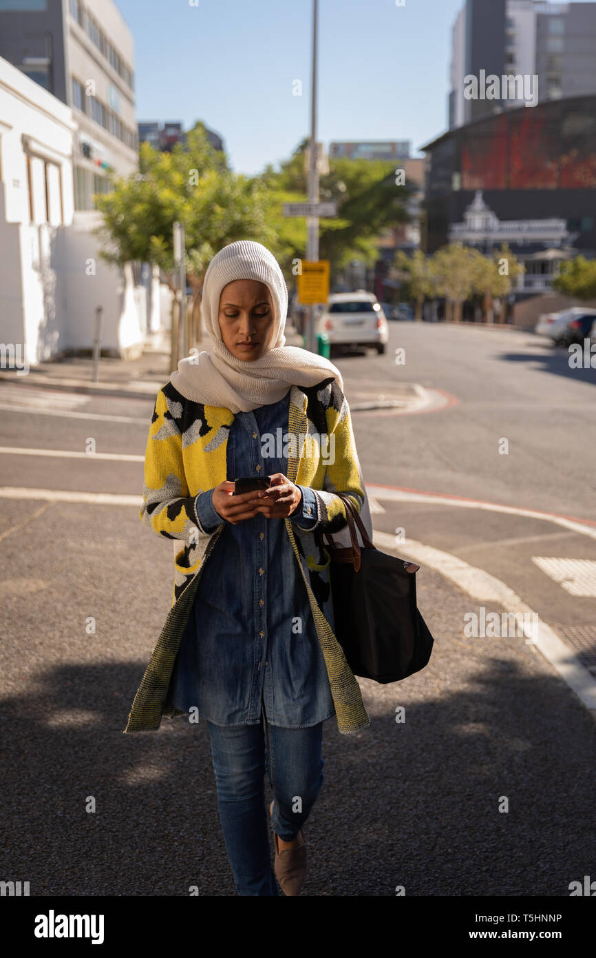 Donna che utilizza il telefono cellulare mentre si cammina lungo la strada Foto Stock