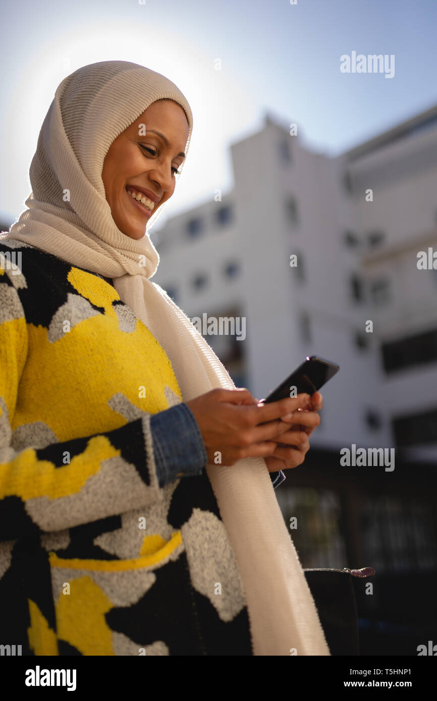 Donna che utilizza il telefono cellulare mentre si cammina per strada in una giornata di sole Foto Stock